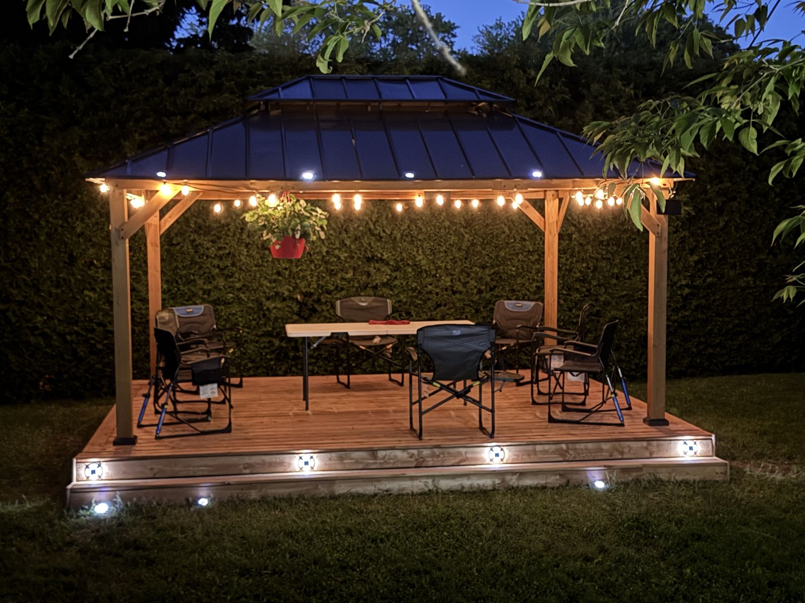 Pavillon de jardin éclairé au-dessus d'un patio en bois, le soir