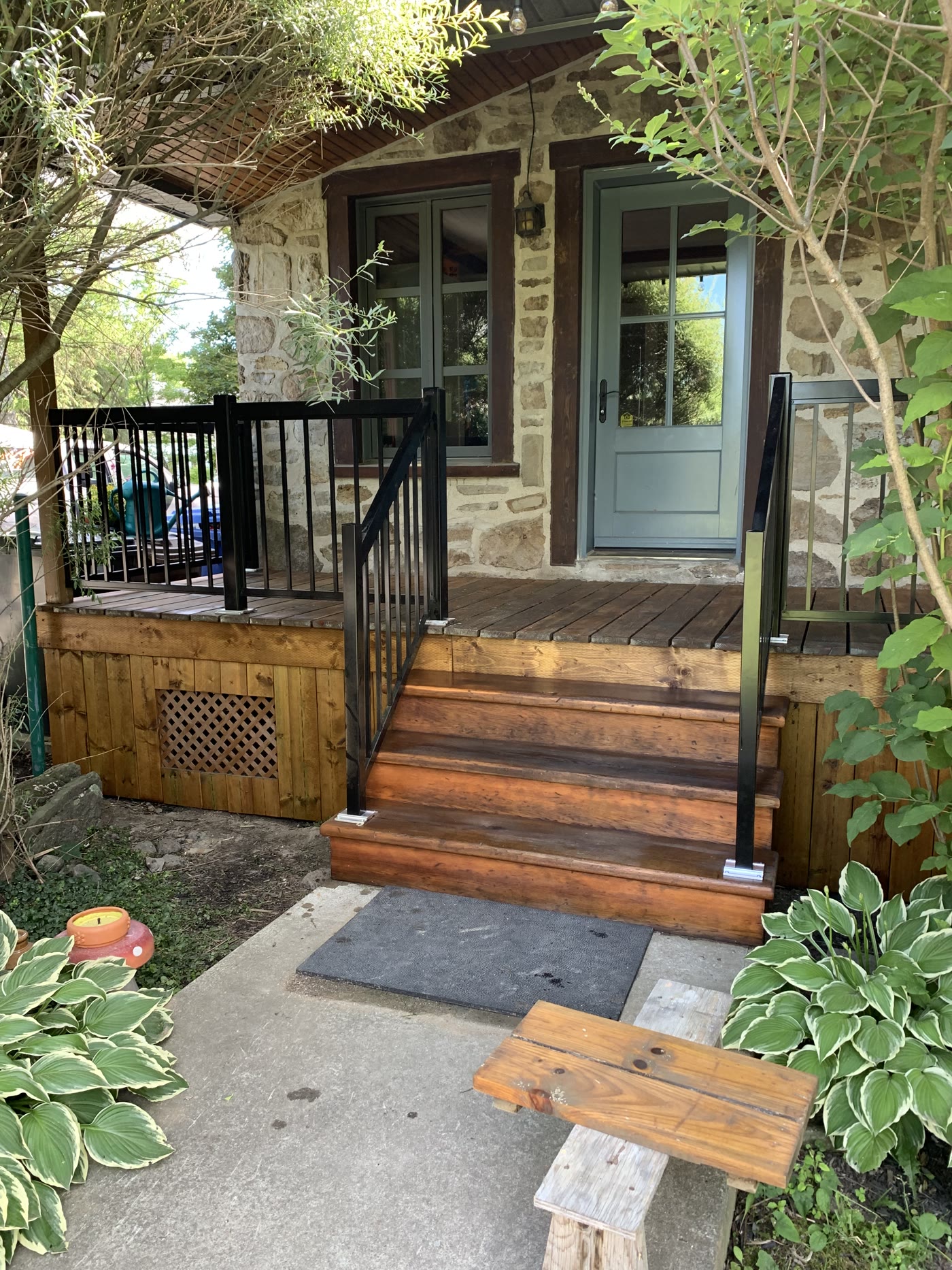 Escalier de bois teint avec rampe d'aluminium noire devant une maison en pierre